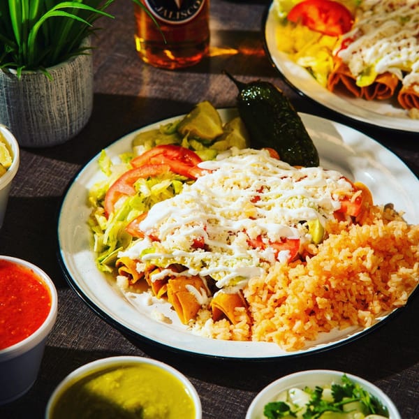 A plate of Chelito's taquitos with rice, lettuce, tomatoes, cheese, and sour cream.