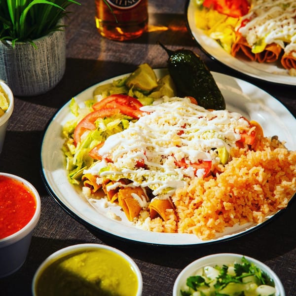 A plate of Chelito's taquitos with rice, lettuce, tomatoes, cheese, and a jalapeño.