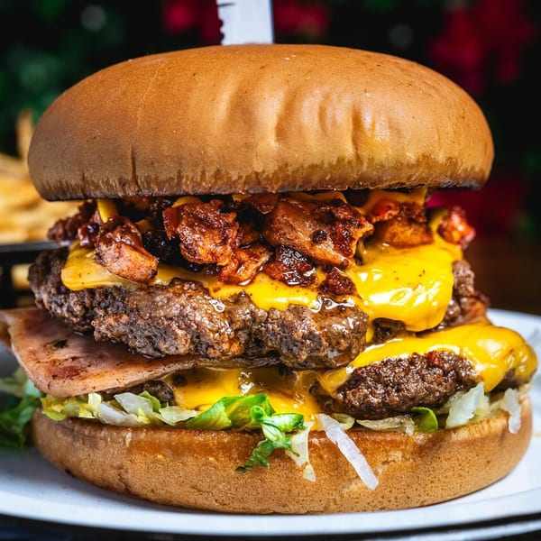 A Chelito's double cheeseburger with bacon, lettuce, and a knife piercing the top bun.