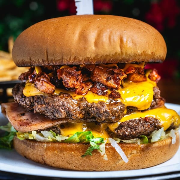A large Chelito's burger with two patties, melted cheese, bacon, and chili, on a white plate.