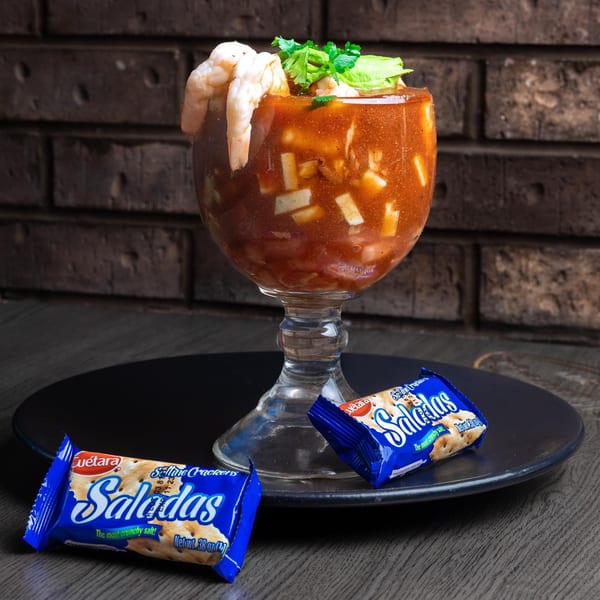A Chelito's shrimp cocktail in a goblet, garnished with cilantro and avocado, served with Saladas crackers.