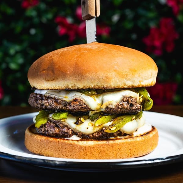 A Chelito's double patty burger with melted cheese and green chiles, skewered with a knife.