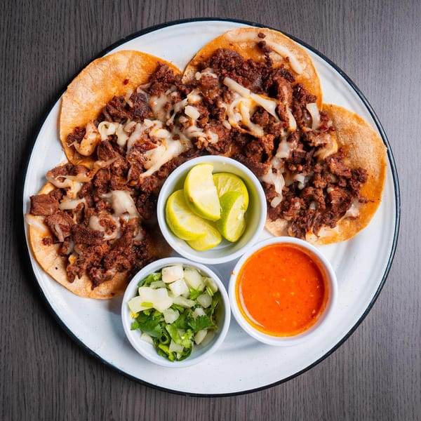 Three Chelito's tacos with meat and melted cheese, served with lime, chopped onions, cilantro, and red sauce.
