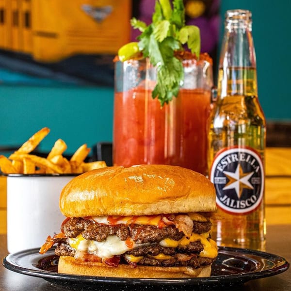 A Chelito's triple cheeseburger with bacon, fries, a Michelada, and an Estrella Jalisco beer.