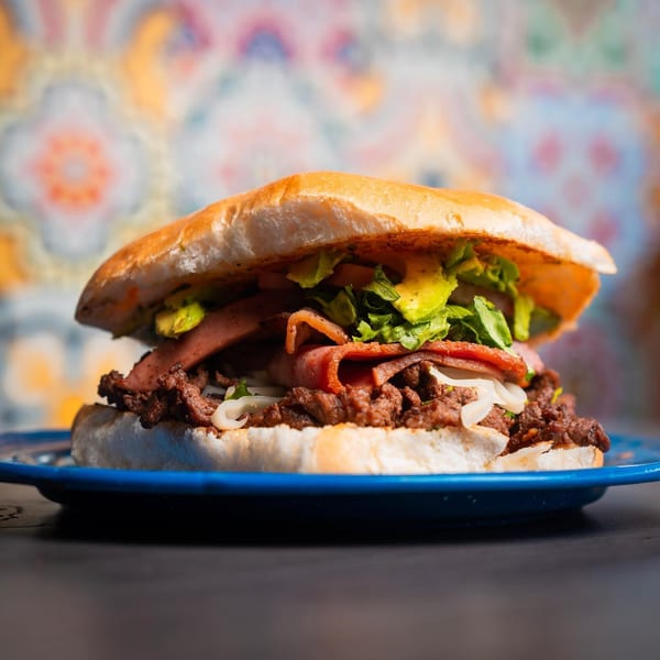 A Chelito's burger with beef, bacon, avocado, lettuce, and onions on a blue plate.