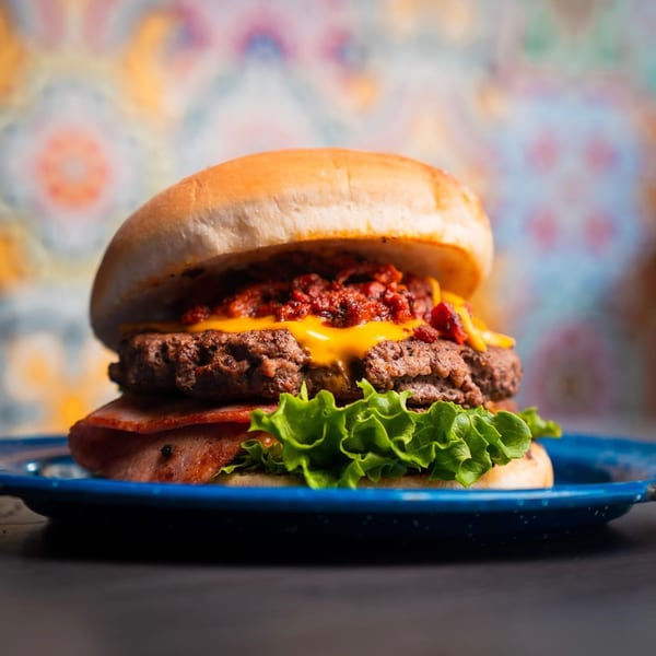 A Chelito's burger with chili, cheese, bacon, and lettuce on a blue plate.