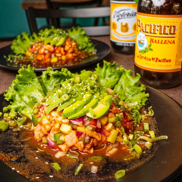 Two plates of ceviche with avocado, lettuce, and green onions, with two beer bottles in the background.