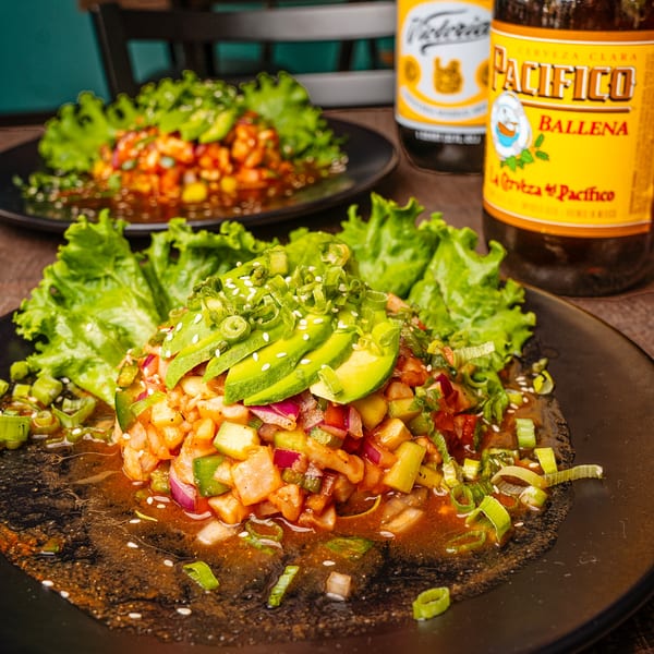 Two plates of ceviche with avocado, lettuce, and green onions, with two beer bottles.