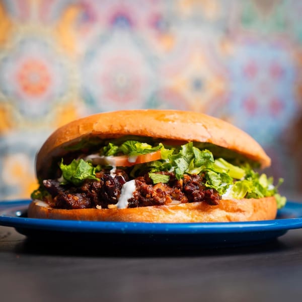 A Chelito's burger with shredded meat, lettuce, tomato, and white sauce on a blue plate.